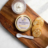 Ars Italica Caviar gourmet caviar, styled on a wooden cutting board with a small glass bowl of white cream, mother of pearl spoon, and blinis.