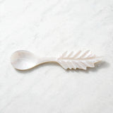 A mother-of-pearl spoon with a leaf-shaped handle, resting on a light gray marble surface.